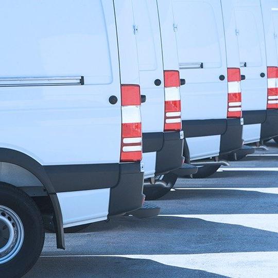 Close-up image of the back tail lights of four white vans